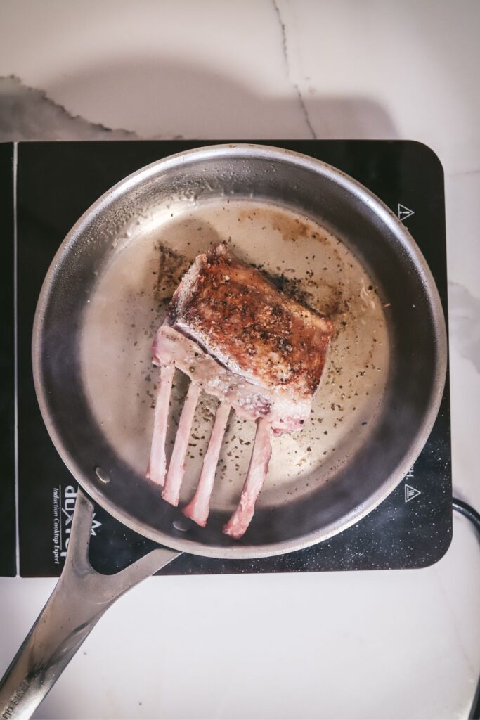 Rack of lamb, one side seared, the other side searing. 