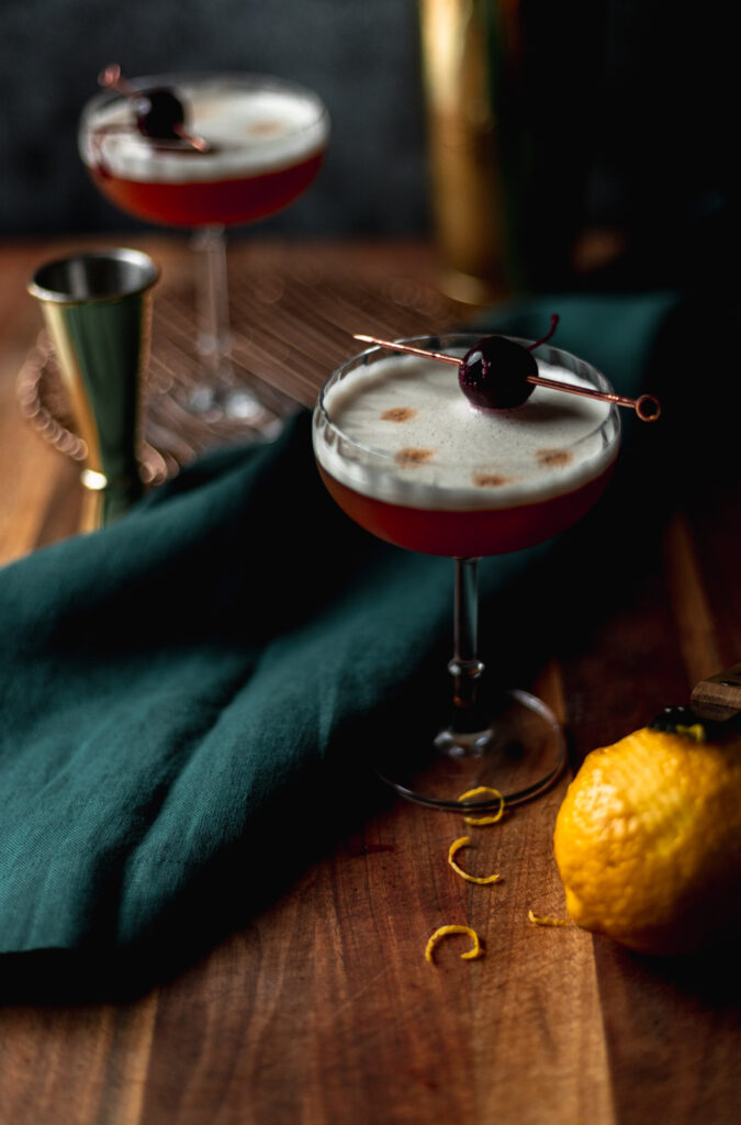 Two amaretto sours on a cutting board with cherry garnish