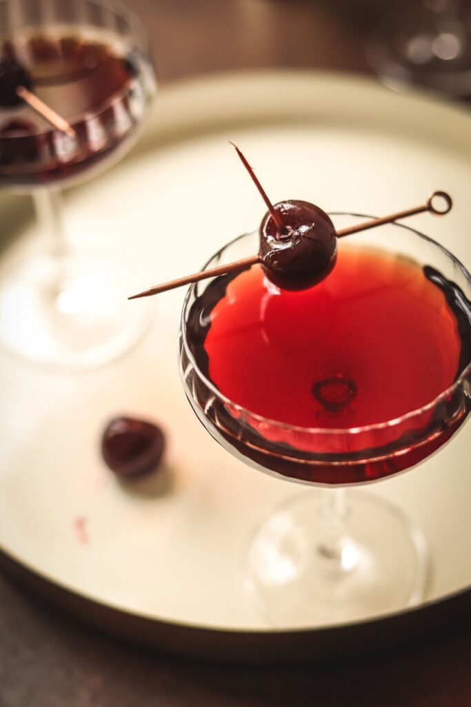 A single Manhattan cocktail on a serving tray, garnished with cherry.