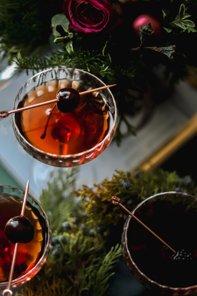 A manhattan cocktail surrounded by evergreen.