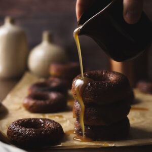 A photo of the best baked doughnut recipe, including three sticky toffee doughnuts with sauce being poured on them