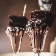 A photo of two chocolate cake milkshakes with a slice of chocolate cake on top