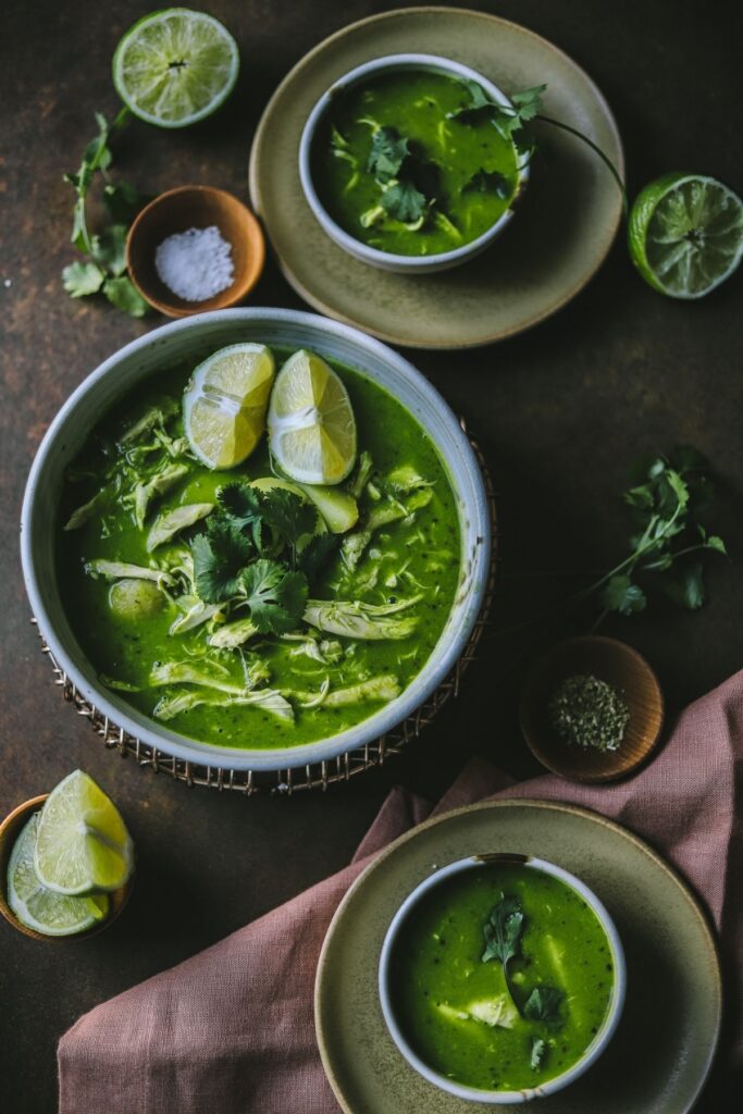 A photo of cilantro chicken soup garnished with limes