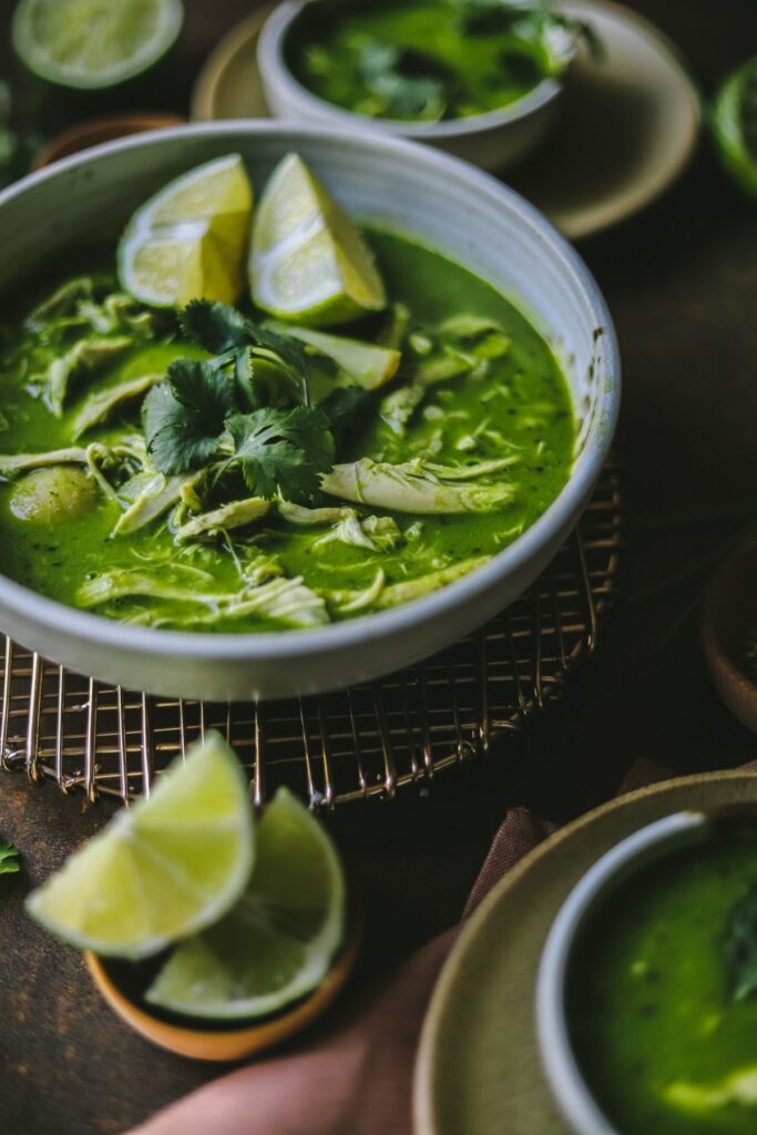 A photo of cilantro chicken soup garnished with limes