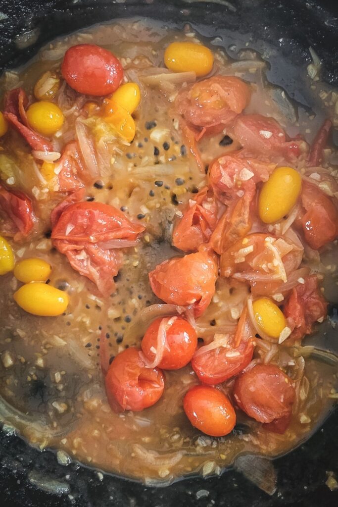 A photo of cherry tomatoes and champagne reducing in a cast iron skillet