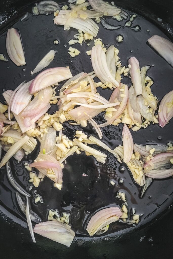A photo of garlic and shallots cooking in a cast iron skillet