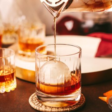 A maple old fashioned being poured over a large ice cube.