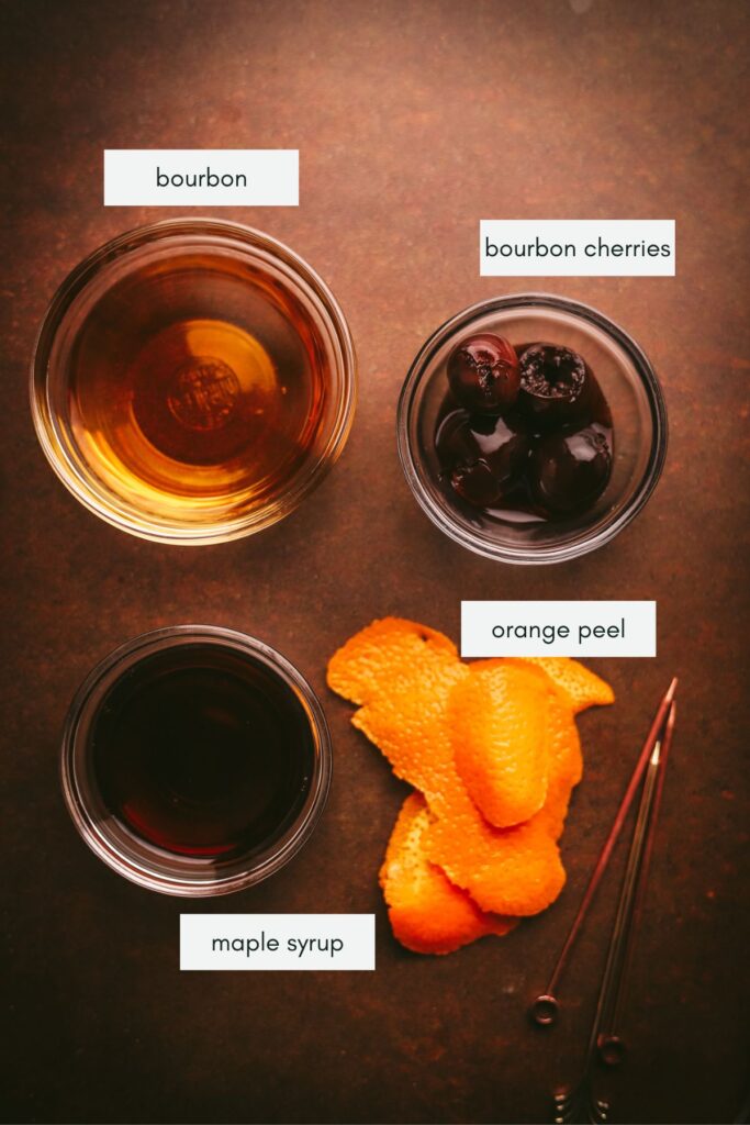 Ingredients for a maple old fashioned: maple syrup, whiskey, bourbon cherries, orange peel. 