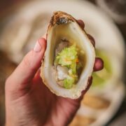 A photo of someone holding an oyster on the half shell with tomatillo habanero mignonette