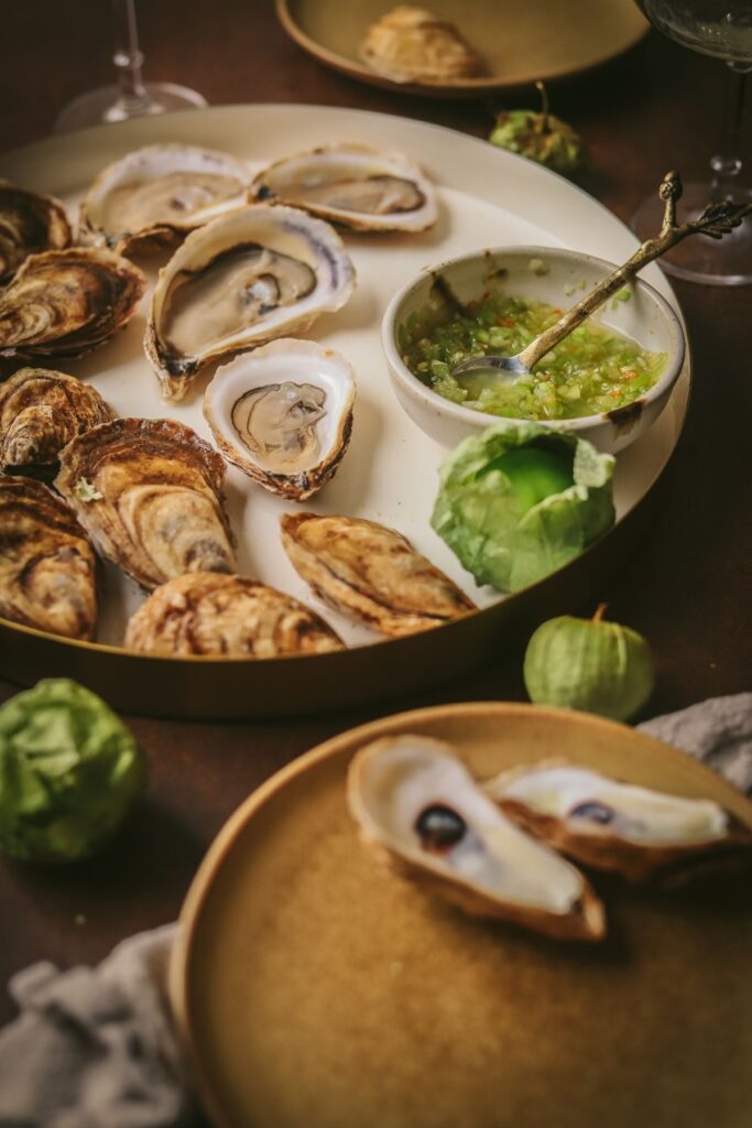 A photo of oysters on the half shell with tomatillo habanero mignonette in a small bowl.