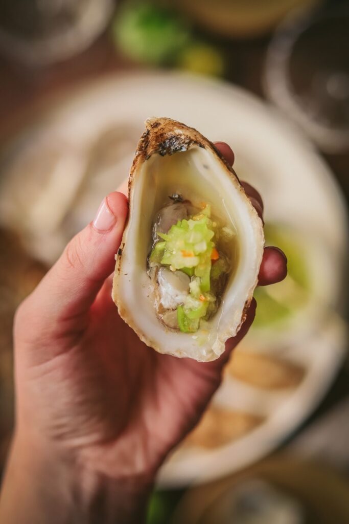 A photo of someone holding an oyster with tomatillo habanero mignonette