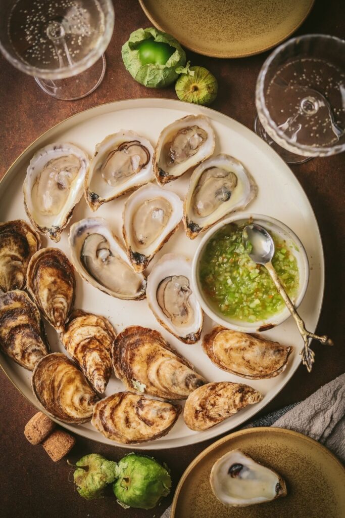 A photo of oysters on the half shell with tomatillo habanero mignonette in a small bowl.