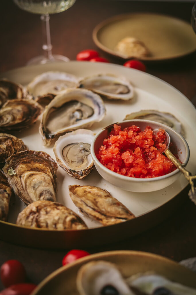 A photo of multiple oysters with tomato and vermouth granita garnish