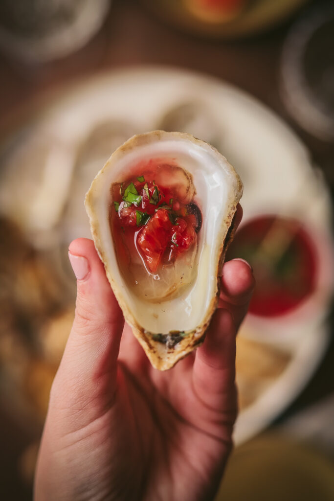a person holding an oyster with champagne mignonette and blood orange