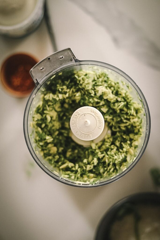 Food processor with arugula and almonds blended together.