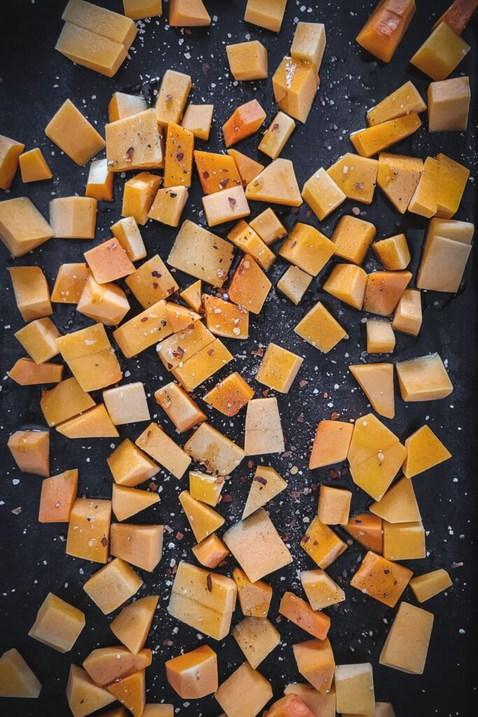 Baking sheet filled with cubed butternut squash and hot pepper flakes