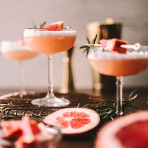 Three grapefruit cocktails with gin surrounded by grapefruit and rosemary