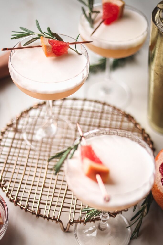 Three grapefruit cocktails with gin surrounded by grapefruit and rosemary