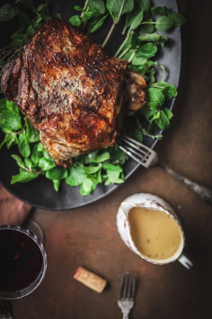 A photo of slow roasted leg of lamb with a glass of red wine and rosemary gravy