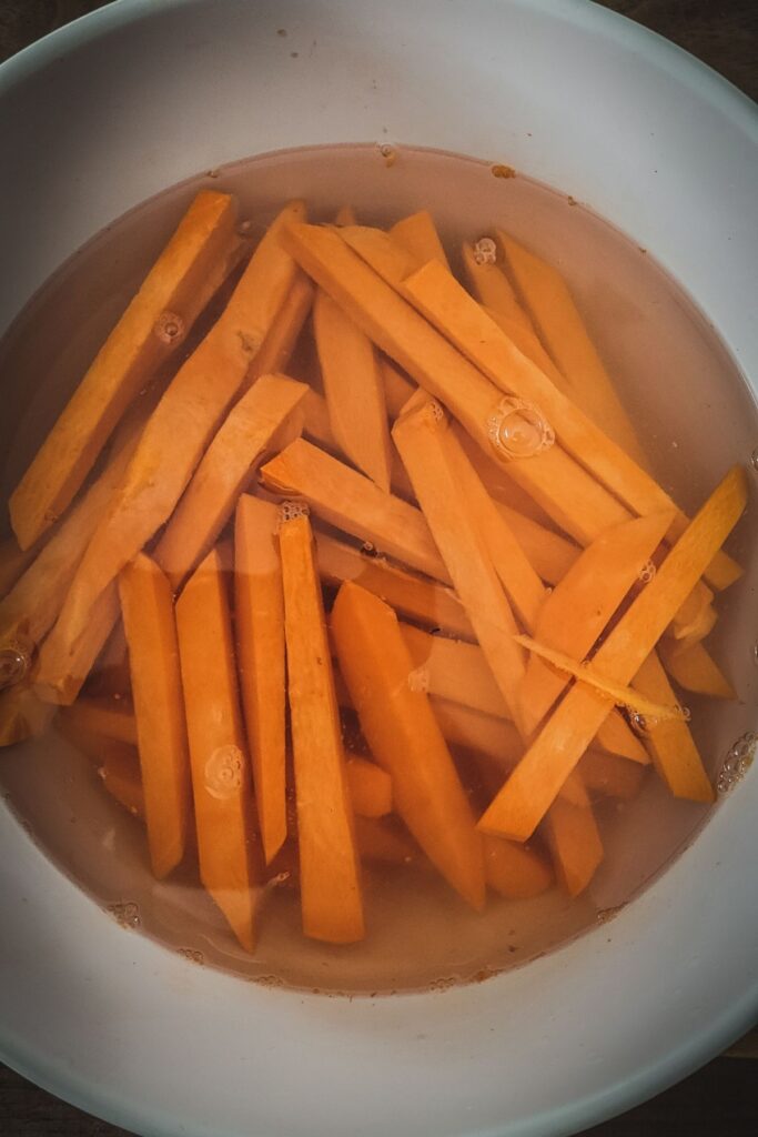 A photo of raw sweet potato fries being soaked in a bowl of water.