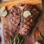 A photo of a perfectly grilled t-bone steak with compound butter and asparagus.