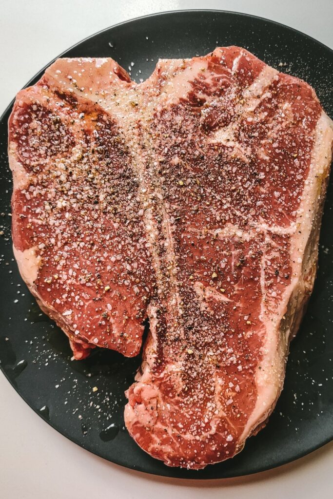 A t-bone steak seasoned with salt and pepper before it goes on the grill. 