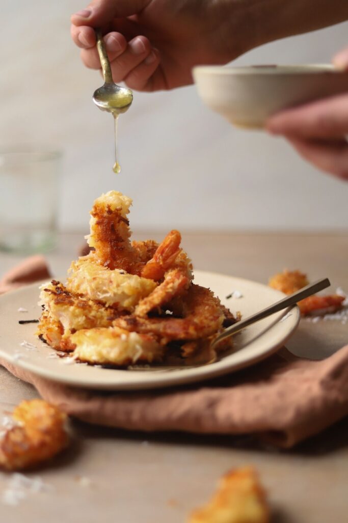 A plate of coconut shrimp with honey sauce being drizzled over the top.