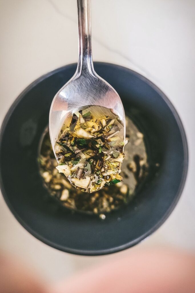 A photo showing chopped rosemary, garlic and oil in a spoon.