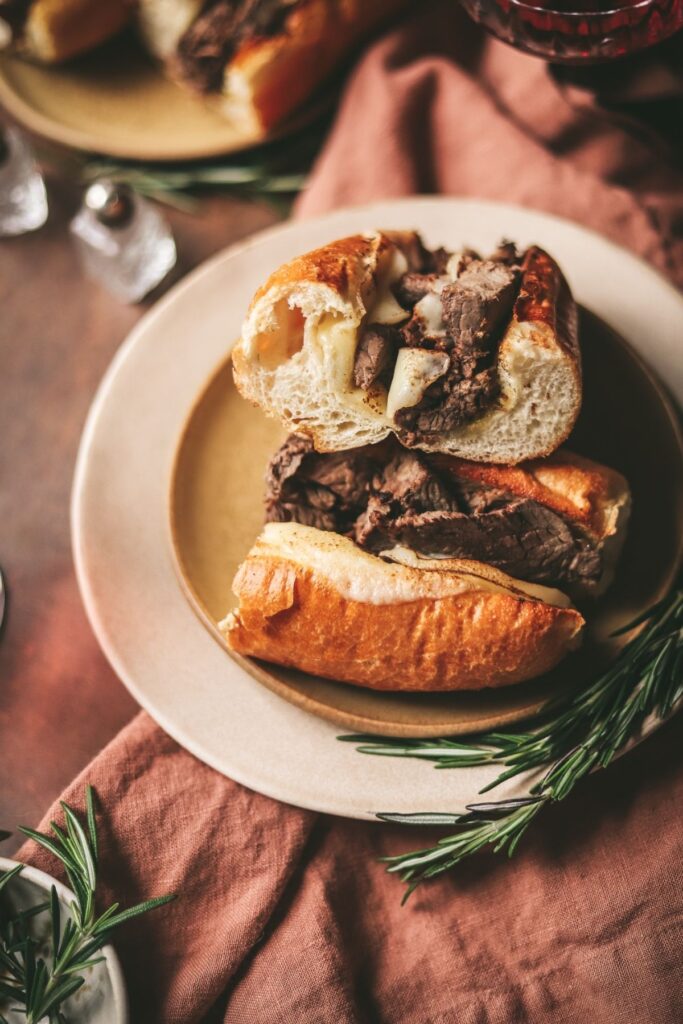 A photo of two french dip sandwiches with red wine. 