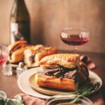 A french dip sandwich surrounded by rosemary and red wine.
