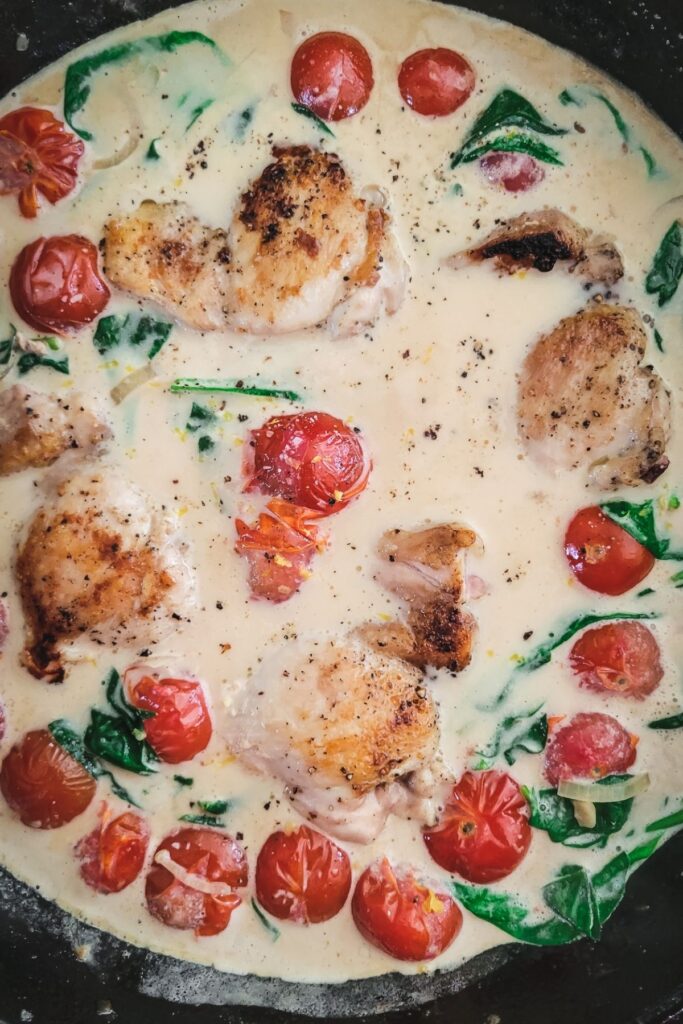 adding the chicken thighs back to the skillet with tomatoes, cream and spinach. 