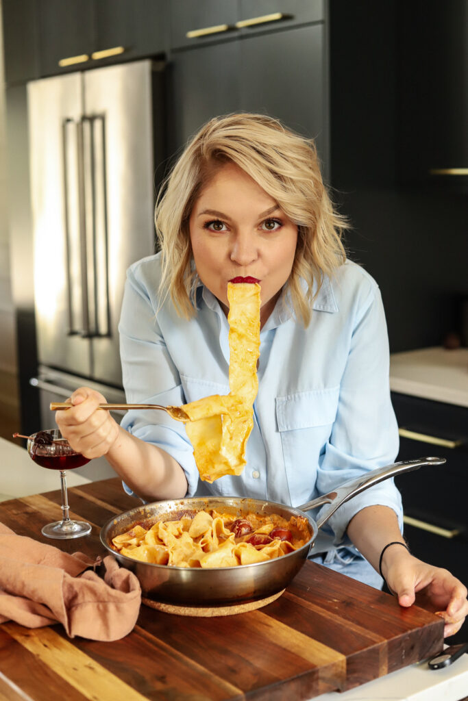 A photo of Cara Campbell of the Gourmet Bon Vivant, slurping pasta in her kitchen, straight from the pan. 