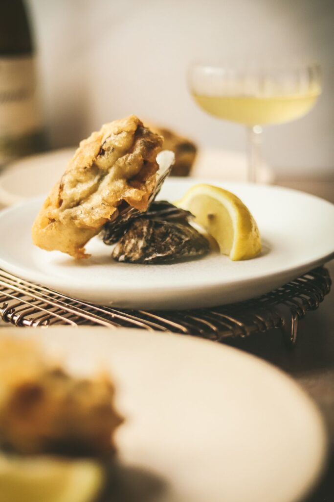 A fried oyster plated with its shell and a glass of wine.