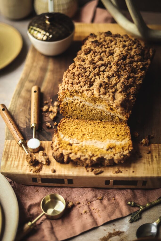 a slice of pumpkin cream cheese loaf on a wooden cutting board. 