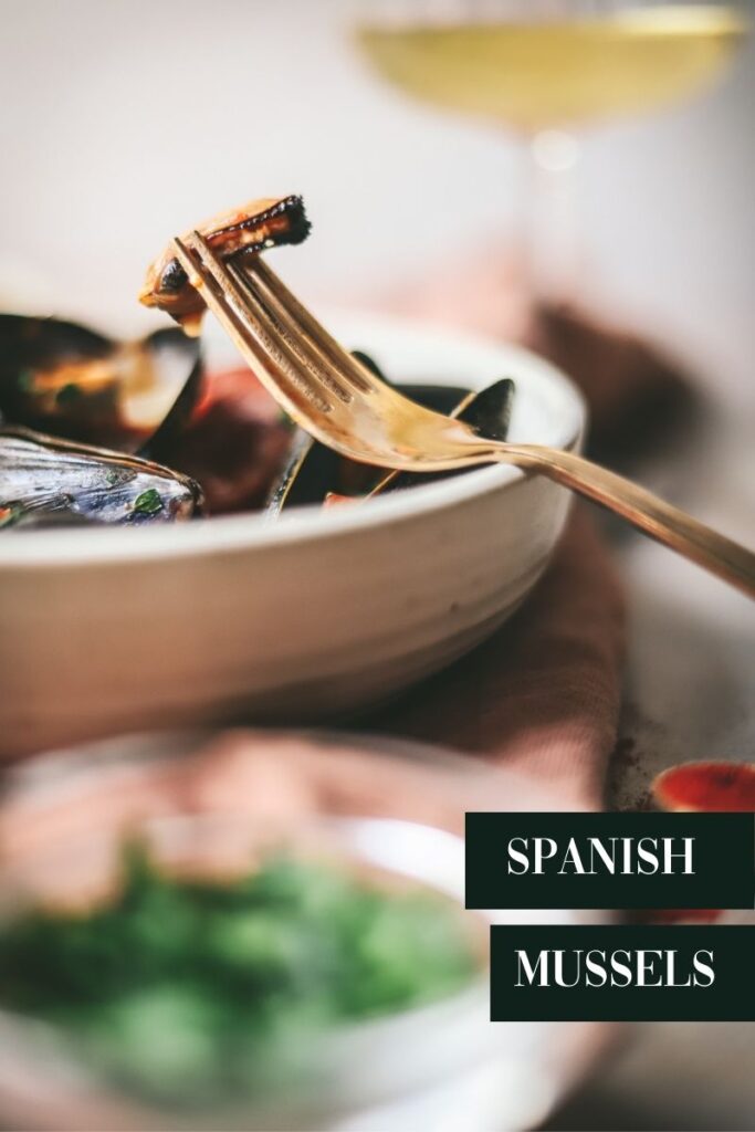 A bowl of Spanish-style mussels with bread, lemons, wine, and title text.