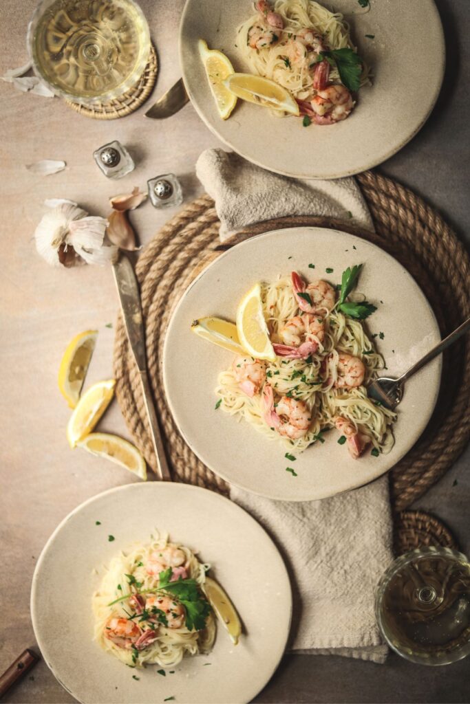 Three plates of shrimp scampi, overhead shot with lemons and wine. 