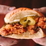 A fried chicken sandwich being held with two hands, pickles on top.