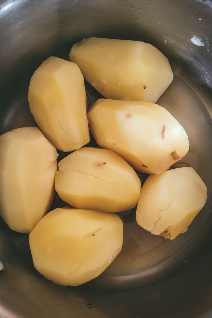 Whole potatoes peeled in pot.