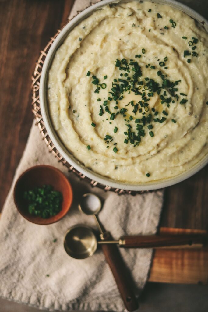 A bowl of mashed potatoes with cheese, butter and chives.