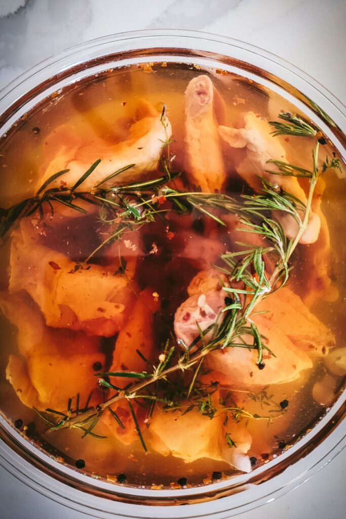 Chicken wing brine with herbs and aromatics in a glass bowl. 