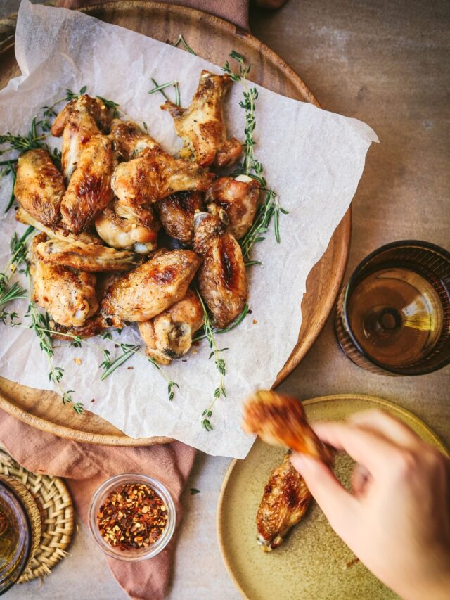 A plate of chicken wings and someone grabbing one.