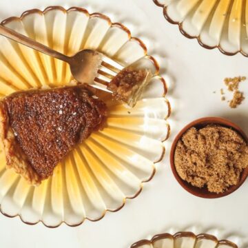 A slice of tarte au sucre on a yellow plate with brown sugar.