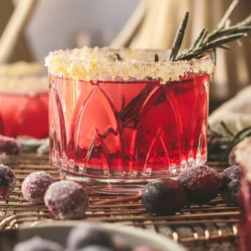 Three cranberry margaritas with christmas trees in the background.