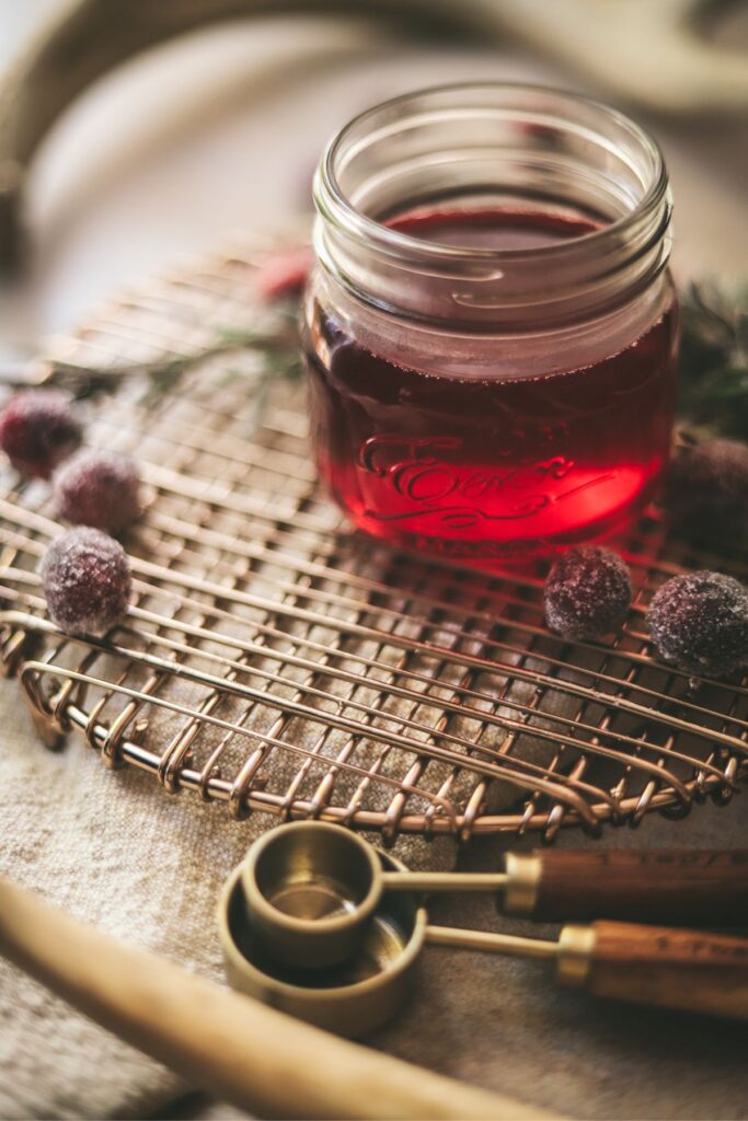 A jar of cranberry simple syrup with frosted cranberries and rosemary. 