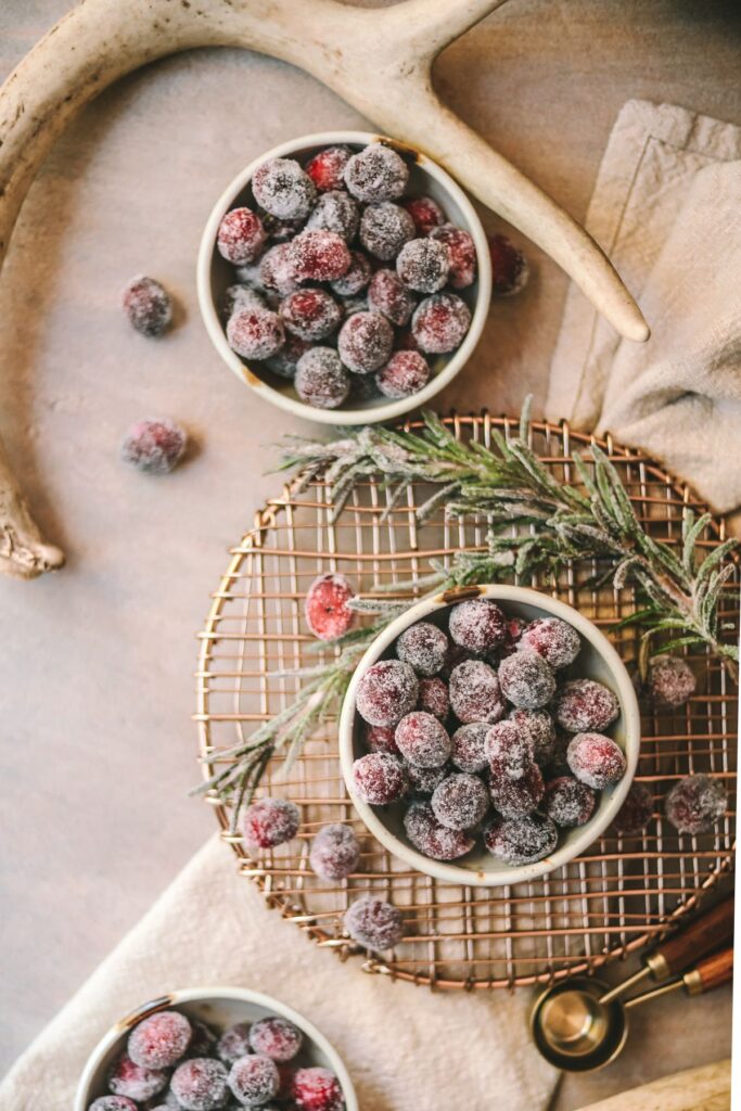 Three bowls of frosted cranberries with rosemary.