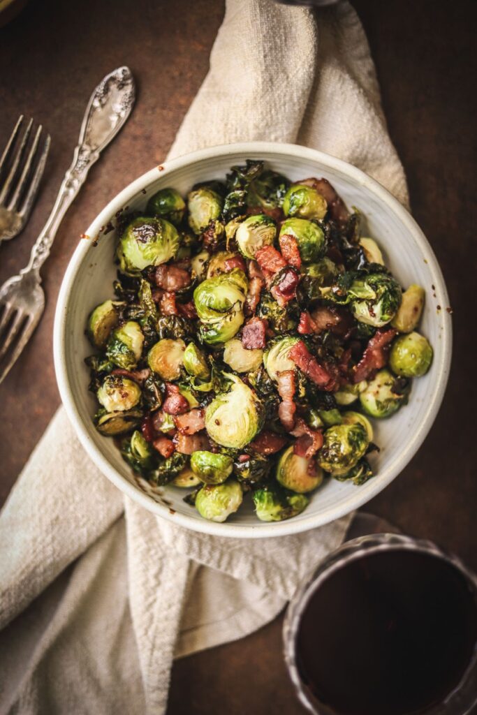 A bowl of raosted brussels sprouts with bacon and a glass of red wine. 