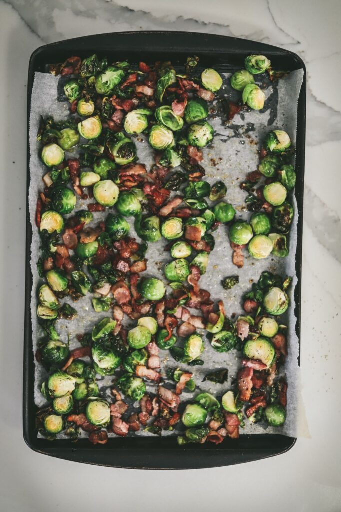 Brussel's sprouts and bacon on a baking sheet after they've roasted.