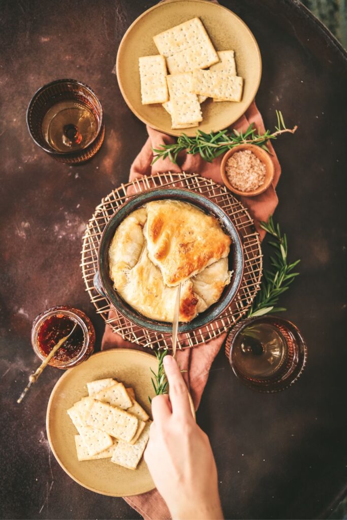 Baked brie with a hand reaching in for a scoop.