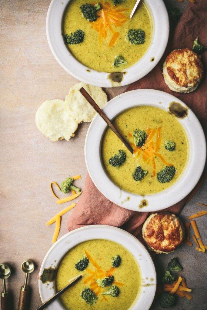 three bowls of broccoli cheddar soup with biscuits.