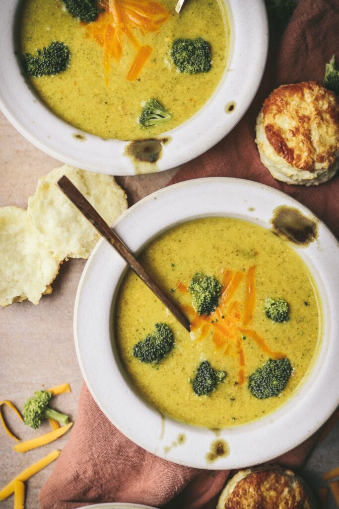 Two bowls of broccoli cheddar soup with biscuits.